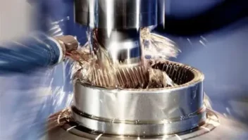 A close up image of a drilling machine working on a gear with water flowing to move debris.